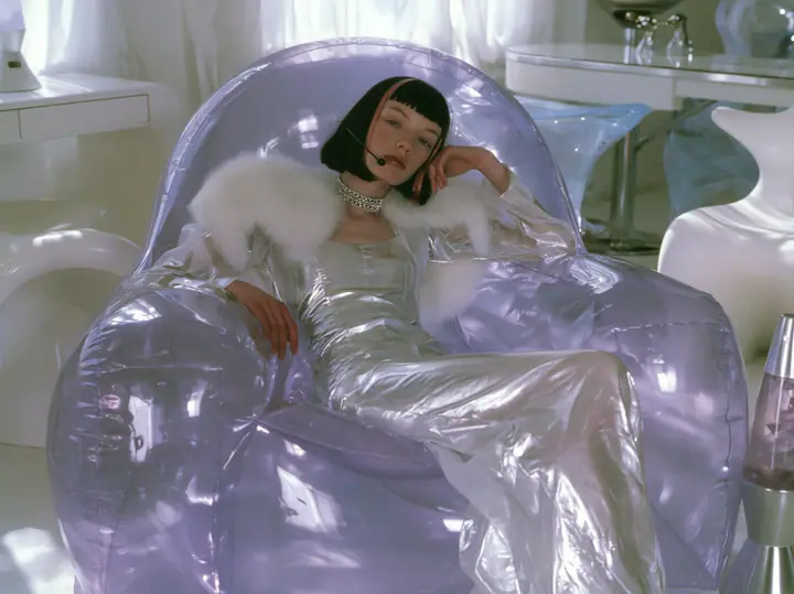 Y2K high fashion editorial, a 2001 couture magazine story: a young Caucasian American woman with pale skin and a glossy black blunt bob with heavy straight bangs and one clay-orange streak, a thin black headset…